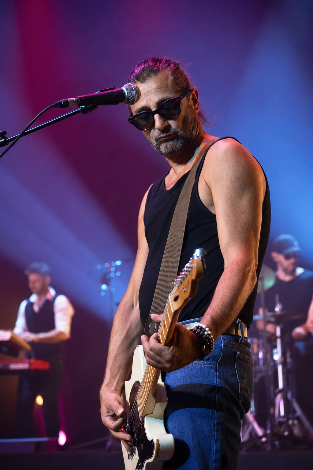 Guitariste de Victoria Orka au micro, cheveux longs et lunettes noires, sous une lumière de scène violette.